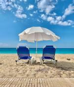 Dwa leżaki i parasol stojące na plaży, w tle błękitne niebo